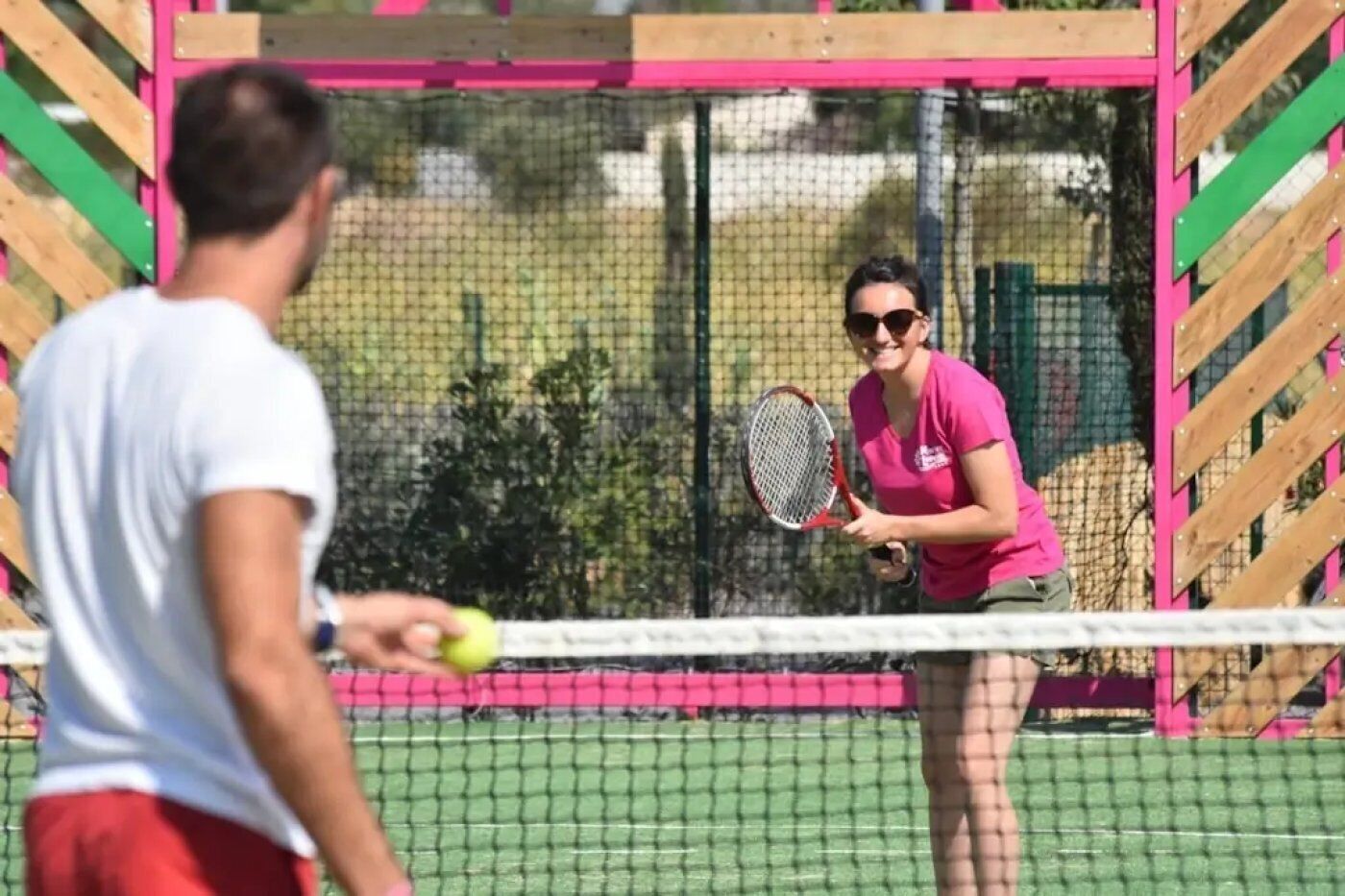 A tennis court with a net, a player in a pink shirt, and another player in a white shirt.