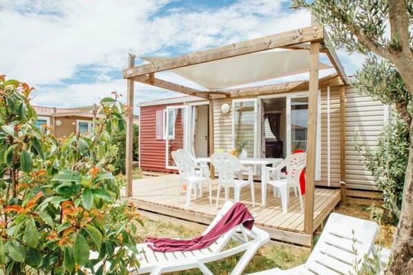 A covered outdoor area with a table and chairs, a wooden deck, and a view of a red building.