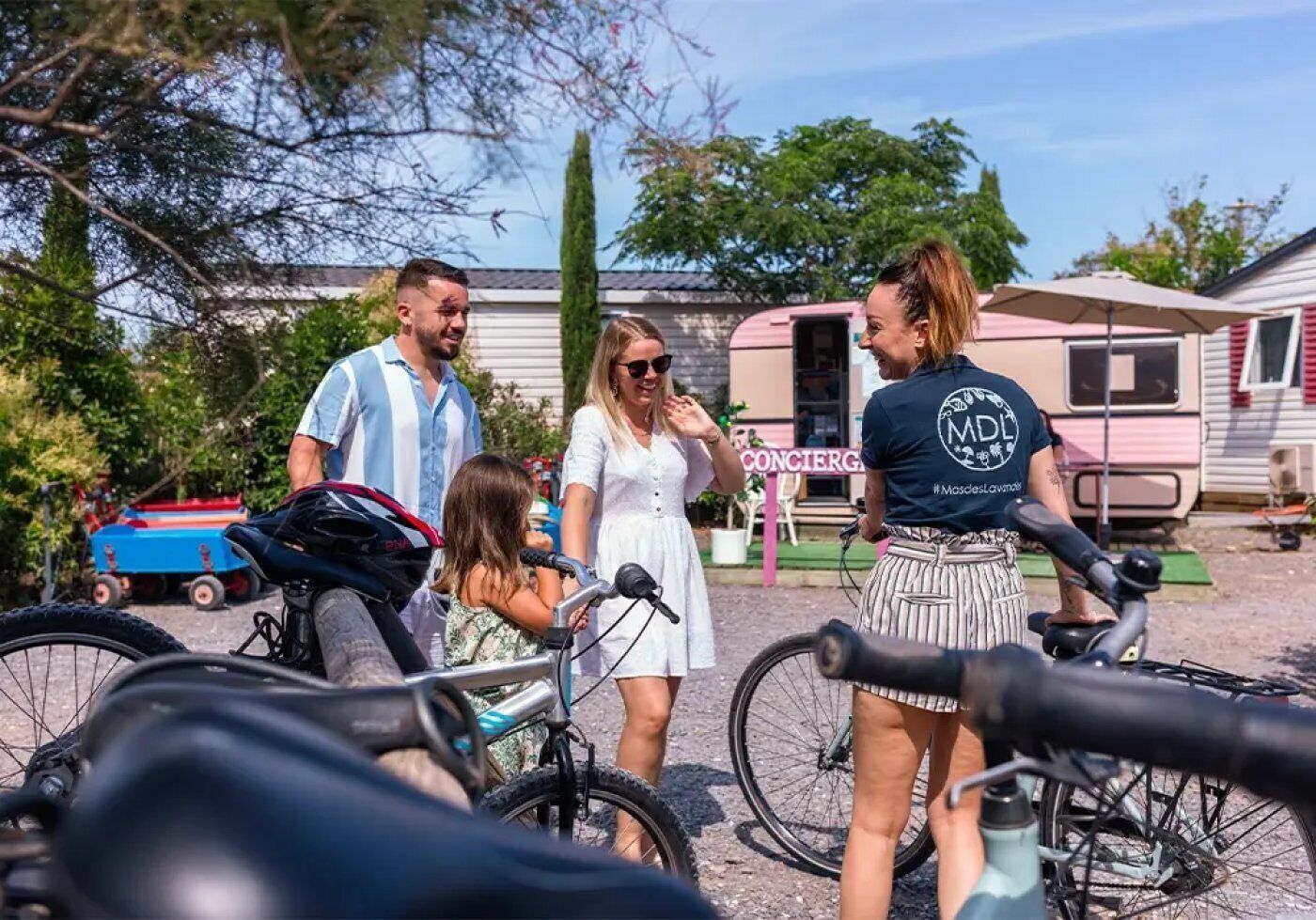 Eine Gruppe von Personen steht draußen mit Fahrrädern, einem Anhänger und einem Auto im Hintergrund.