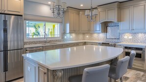 A modern kitchen with a large island, stainless steel appliances, and a view of a green outdoor area.