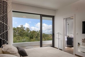 A modern bedroom with a large sliding glass door leading to a balcony, a bed with a view, and a walk-in closet.
