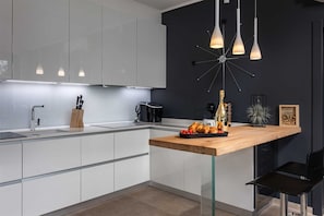 Una cocina moderna con armarios blancos, encimera de madera y una silla negra.