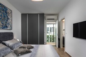 A bedroom with a bed, pillows, a wardrobe, a TV, and a balcony with a view.