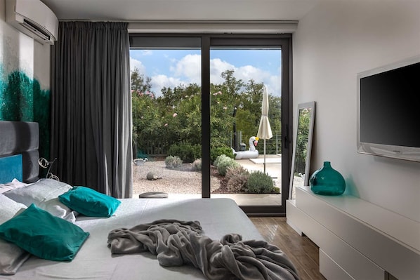 Habitación de hotel moderna con cama, televisión, ventana grande y vistas al jardín.
