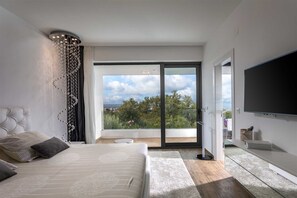 Un dormitorio moderno con una cama grande, televisión y balcón con vista a la ciudad.