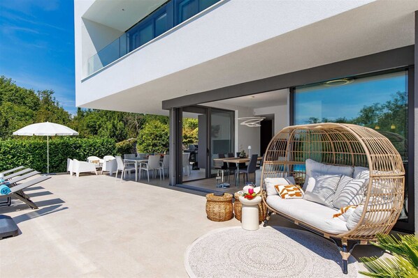 A modern outdoor living area with a glass-enclosed dining space, a wicker sofa, and a poolside lounge. - Villa LUXOR with heated pool (Sveti Vid Miholjice)