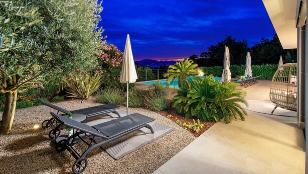 A poolside area with lounge chairs, umbrellas, and a view of the mountains at dusk.