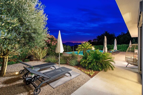 Zona junto a la piscina con sillones, sombrillas y vistas a las montañas al atardecer.