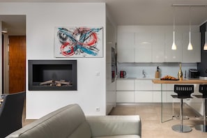 Een moderne keuken met witte kasten, een inbouwoven en een zithoek met een grijze bank en een kleine tafel.