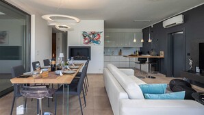 A modern kitchen with white cabinets, a dining area with a wooden table, and a living area with a white sofa and blue cushions. - Villa LUXOR with heated pool (Sveti Vid Miholjice)
