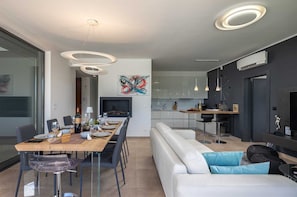 A modern kitchen with white cabinets, a dining area with a wooden table, and a living area with a white sofa and blue cushions.