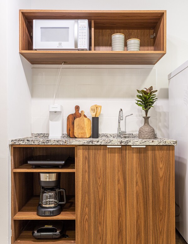 A kitchen with a microwave, coffee maker, and wooden shelves.