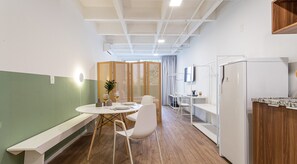 A modern kitchen with a built-in dishwasher, a dining area with a round table and chairs, and a wooden partition with a plant.