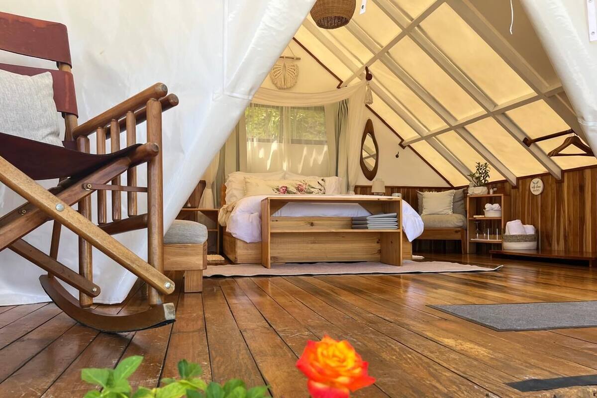 A cozy tented accommodation with a wooden rocking chair, a bed with a floral duvet, and a small wooden side table.