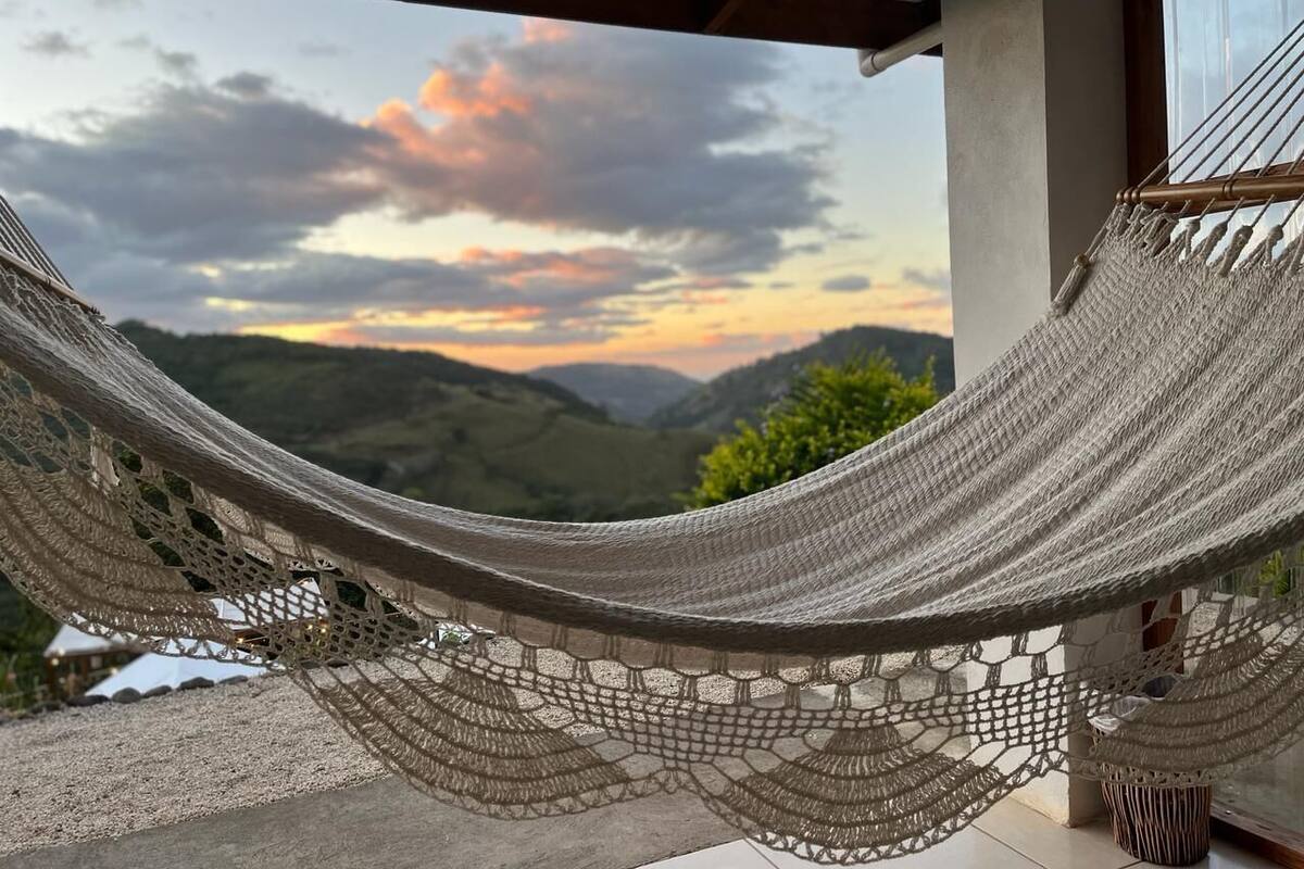 A hammock on a porch with a view of a sunset over hills.