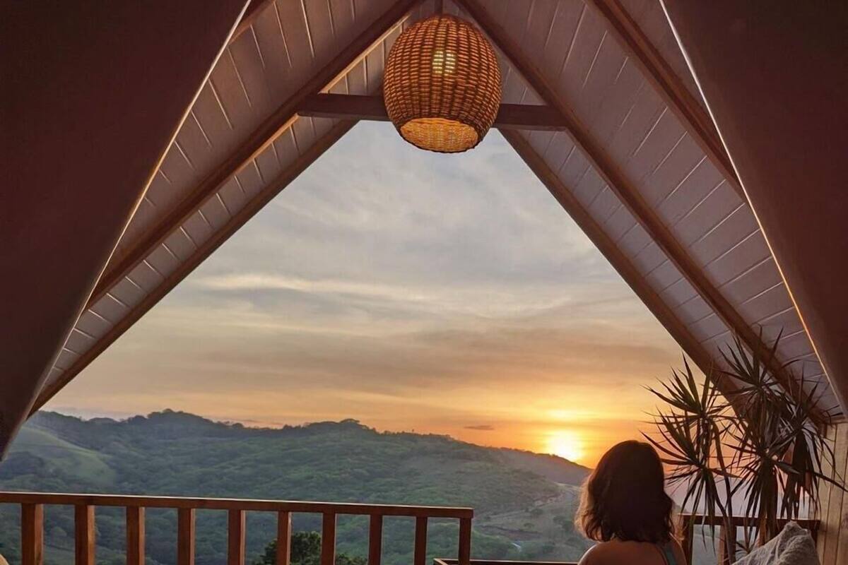 A cozy room with a bed, a small table, and a chair facing a scenic mountain view at sunset.