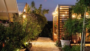 A pathway leading to a building with a slatted facade, surrounded by lush greenery and string lights. - Yaloco House Monteverde  (Sierra)