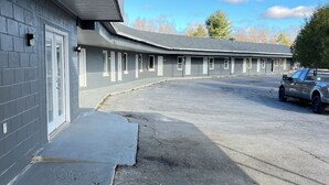 Een motel met een rij kamers, een overdekte parkeerplaats en één geparkeerde auto.