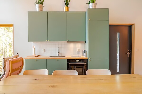 A modern kitchen with green cabinets, a wooden countertop, and a dining area with a table and chairs. - Casa Kolibri, beautiful 3-Bedroom Seaside Cabin in Turku archipelago (Egentliga Finland)
