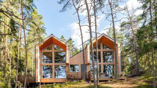 Une cabane aux murs en bois et aux grandes fenêtres, entourée d’arbres.