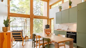 Une cuisine moderne avec des meubles de couleur verte, une table à manger en bois et des chaises. Une grande fenêtre laisse entrer la lumière naturelle et offre une vue sur les arbres.