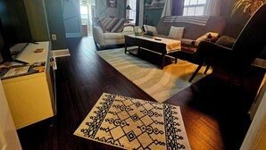 A living room with a sofa, armchair, coffee table, and a patterned rug. - Loft • King Bed • Free Parking • Early Check in 2pm / 12pm Late Check Out (Pottstown)