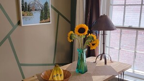 A dining area with a wooden table, a vase with sunflowers, a bowl of bananas, and a painting of a mountain landscape. - Loft • King Bed • Free Parking • Early Check in 2pm / 12pm Late Check Out (Pottstown)