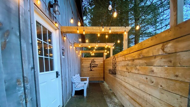 Une façade en bois avec une porte blanche, un banc et des guirlandes lumineuses.