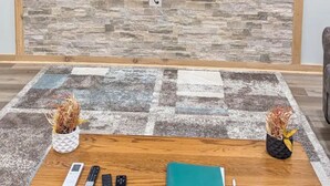 Un salon avec un téléviseur à écran plat fixé au-dessus d’une cheminée, une table en bois sur laquelle reposent des télécommandes, un carnet et des plantes décoratives.