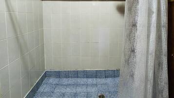 Een douche met een blauw betegelde vloer, houten plafond en een wit douchegordijn.
