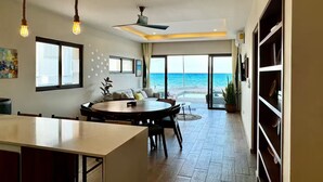 A modern interior with a dining area, a ceiling fan, and a view of the ocean.