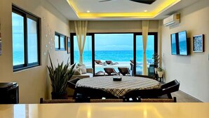 A modern bedroom with a large bed, a ceiling fan, and a view of the ocean.