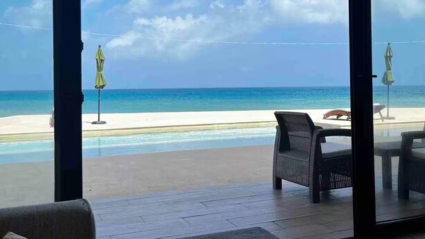 A room with a large glass door leading to a balcony with a view of the beach and ocean.