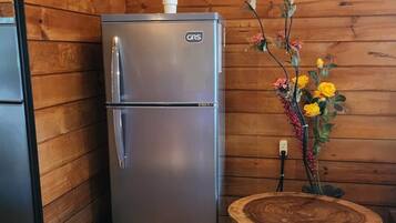 A compact, stainless steel refrigerator with a GRS logo, positioned against a wooden wall.