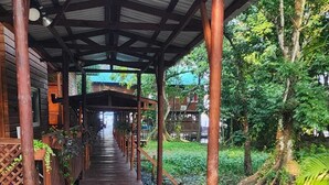 A covered wooden walkway with benches, surrounded by lush greenery and trees.