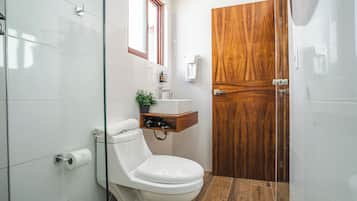 A modern bathroom with a toilet, a wooden vanity, and a glass shower enclosure.