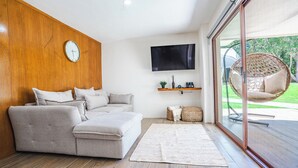 A modern living room with a sofa, a flat-screen TV, a wicker chair, and a large window. - Bungalow with jacuzzi and lake view (Tlajomulco de Zúñiga)