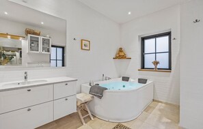 Un baño moderno con un espejo grande, muebles blancos, una bañera independiente y una ventana con vistas.