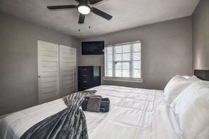 Ein Schlafzimmer mit Bett, Deckenventilator, Fernseher, Fenster mit Jalousien und Kleiderschrank.
