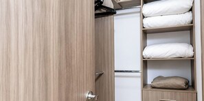 A wooden wardrobe with a mirrored door, a hanging rack, and shelves with folded bedding.