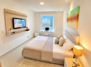 Une chambre moderne avec un lit, une télévision, un bureau avec un ordinateur portable et une fenêtre donnant sur la ville.