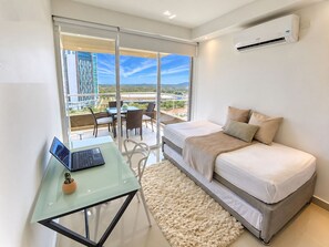 Ein modernes Schlafzimmer mit einem Bett, einem Laptop auf einem Glastisch und Blick auf einen Balkon mit Gartenmöbeln.