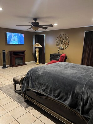 Une chambre à coucher avec un grand lit, une télévision, un ventilateur de plafond, un élément décoratif mural et une cheminée.