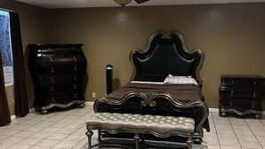 Une chambre à coucher avec un grand lit, un banc, une commode et un ventilateur de plafond.