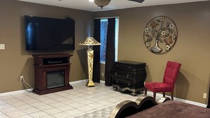 Une chambre à coucher comprenant un lit, un téléviseur, un ventilateur de plafond, un fauteuil rouge, une commode et un élément décoratif mural.