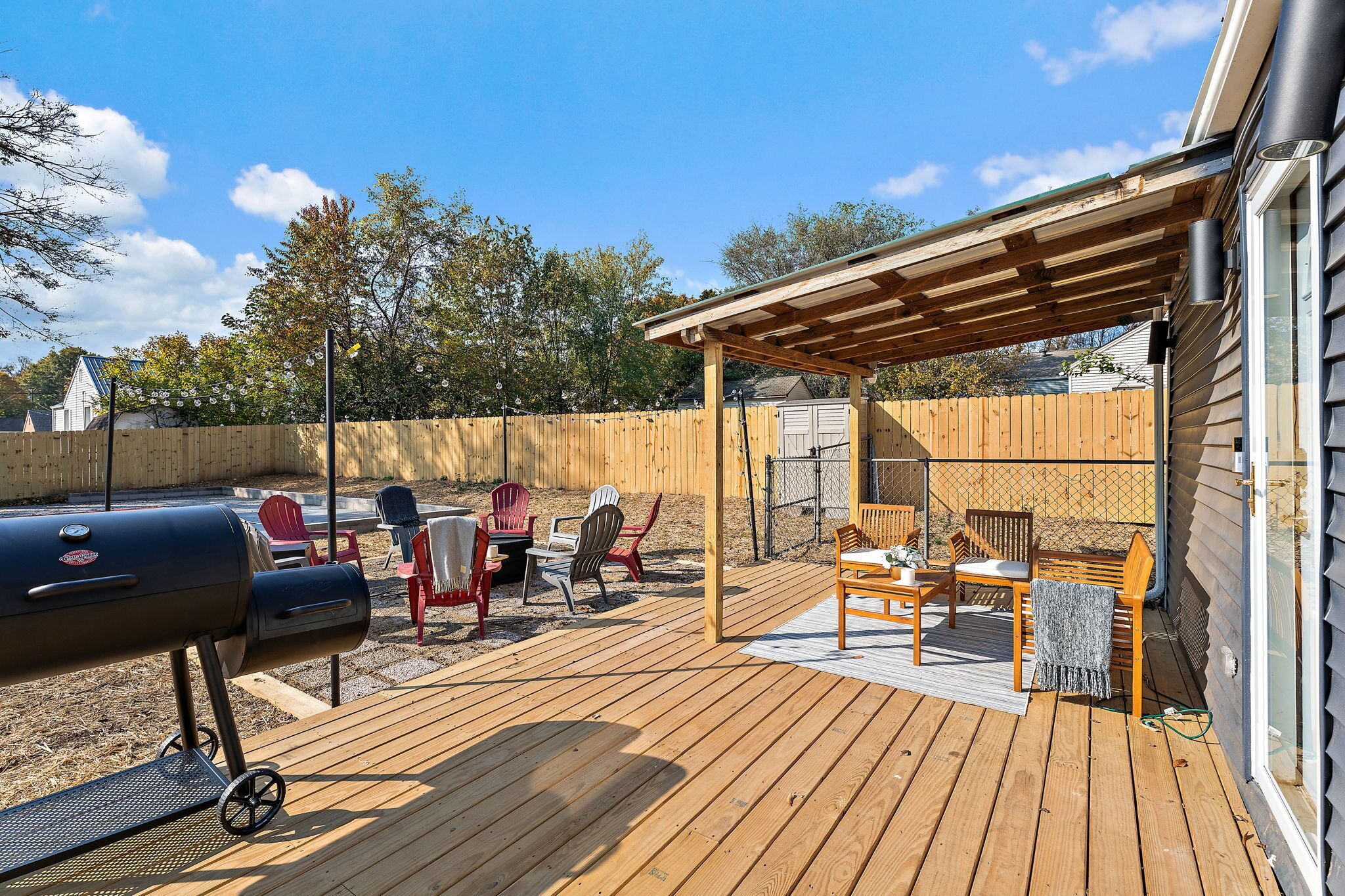 A wooden deck with a grill, outdoor furniture, and a covered seating area.
