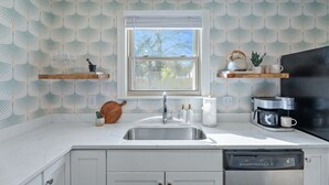 A kitchen with a white countertop, a stainless steel sink, a coffee maker, and a dishwasher.