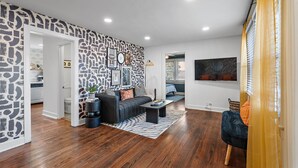 A modern living room with a black and white patterned wall, a dark sofa, a coffee table, and a blue armchair.