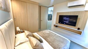 A modern hotel room with a bed, a TV, an air conditioning unit, and a wardrobe. - Apartamentos Mirador - by SOHO (Puerto Colombia)