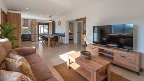 Ein modernes Wohnzimmer mit großem Flachbildfernseher, Holzmöbeln und einem Essbereich mit Tisch und Stühlen.